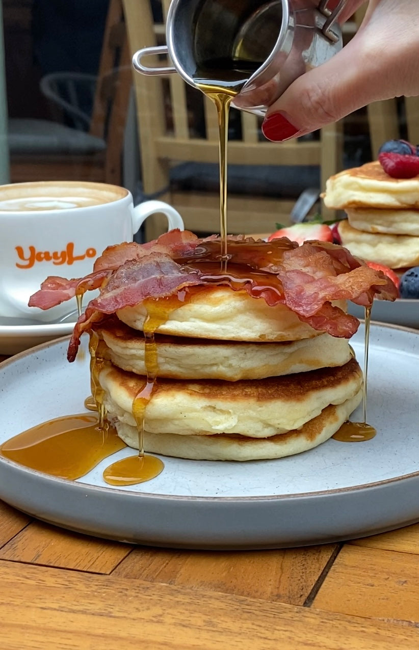 Gluten free pancake stack with crispy bacon and maple syrup, fresh fruit pancake stack in the background